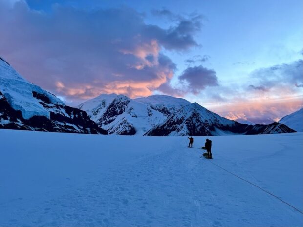 Morning sun illuminates the clouds while climbers pass Kahiltna Dome on the Lower Kahiltna Glacier (Stu Johnson). 