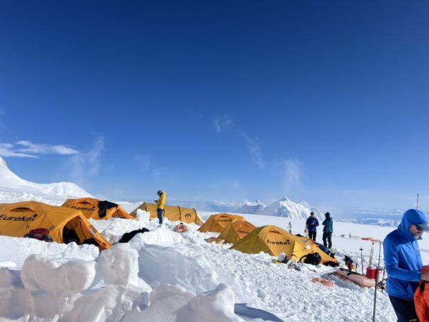 Yellow tents scattered across snow with Mt. Foraker in the background