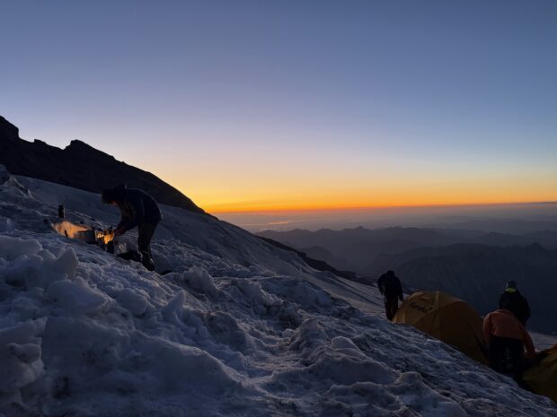 Guides tend a cook stove as the sun sets over Mt. Rainier