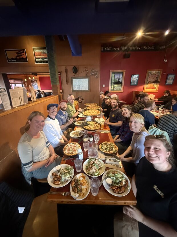 Team 2 sits at a long table sharing pizza in Talkeetna